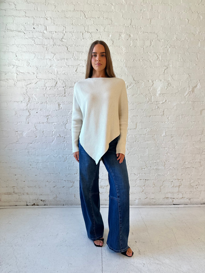 Woman wearing cream long sleeve ribbed sweater with pointed hem, and dark wash jeans. 