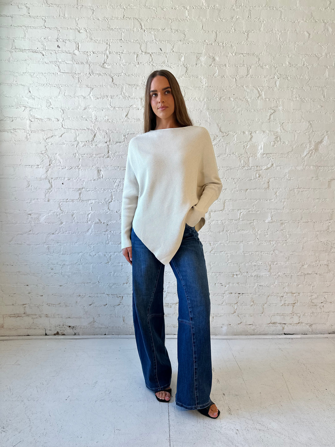 Woman wearing cream long sleeve ribbed sweater with pointed hem, and dark wash jeans. 