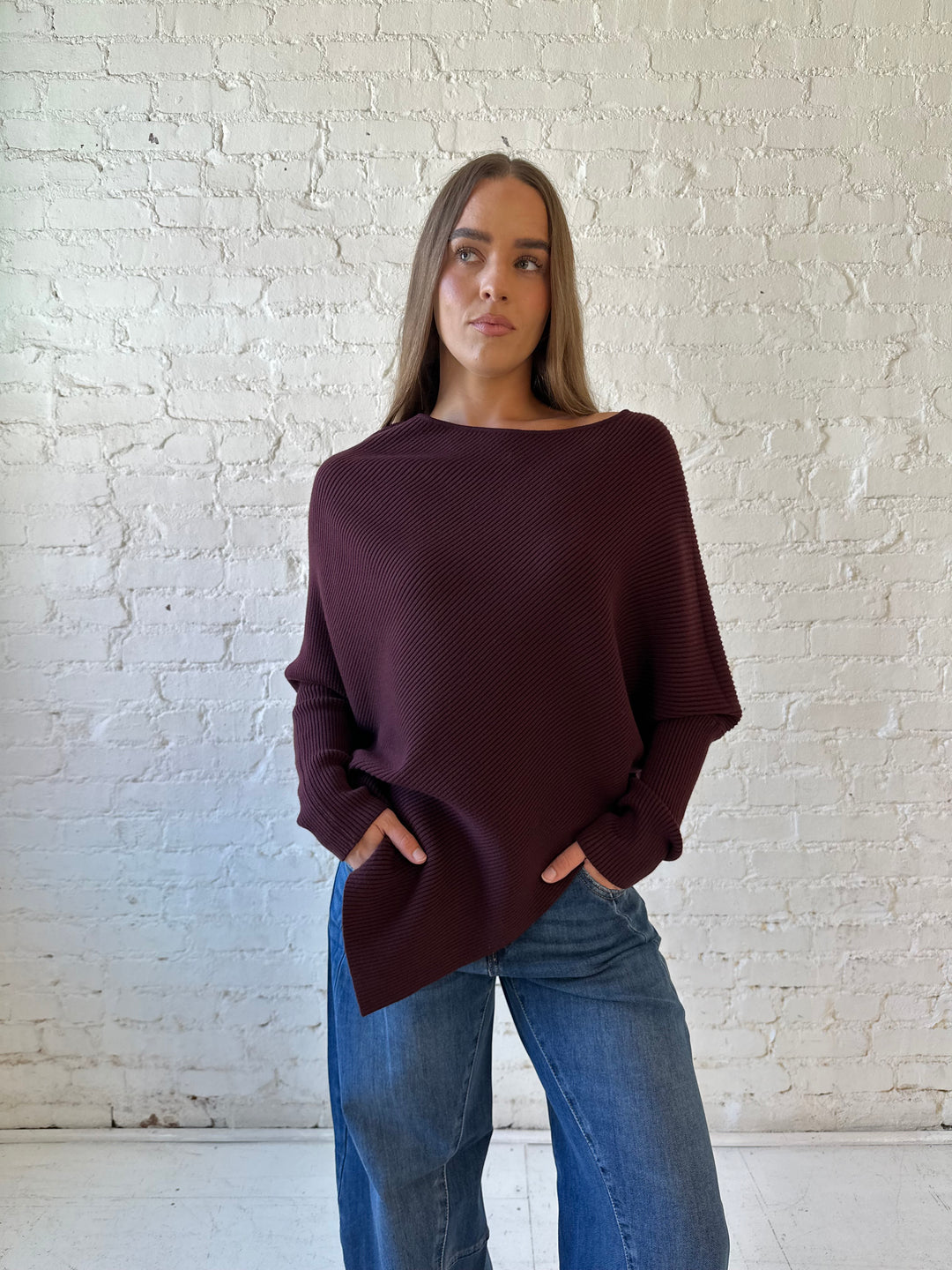 Woman wearing burgundy ribbed long sleeve sweater with pointed hem, and dark wash jean. 