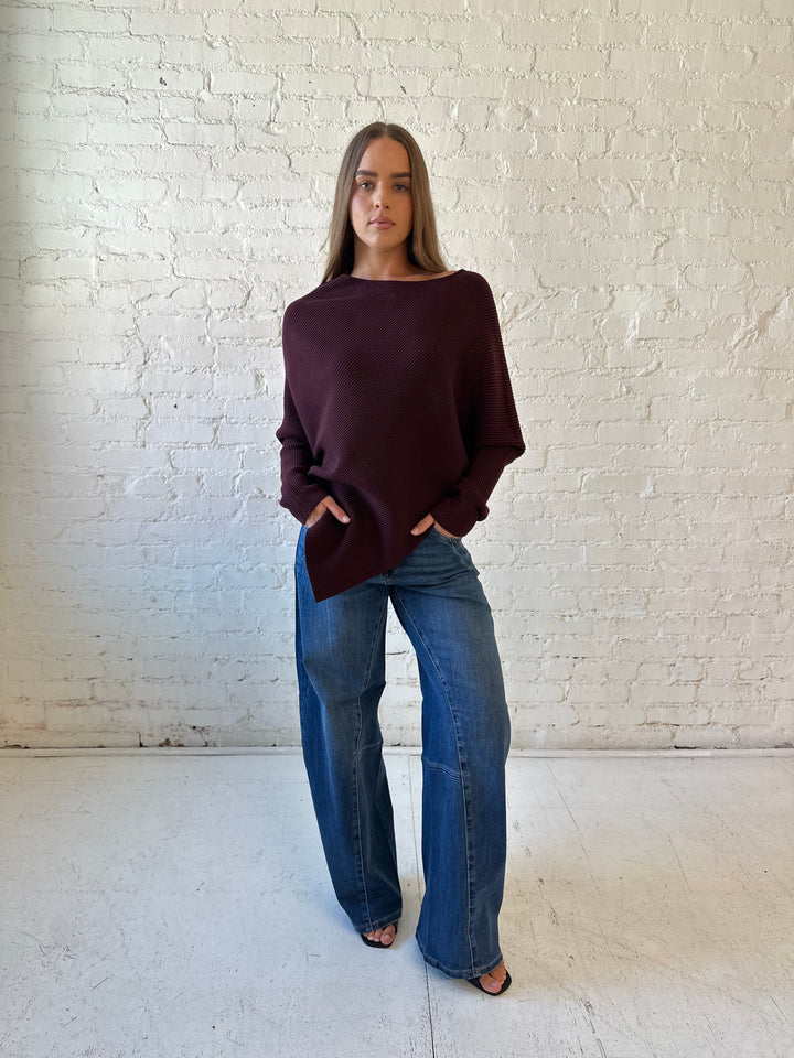 Woman wearing burgundy ribbed long sleeve sweater with pointed hem, and dark wash jean. 