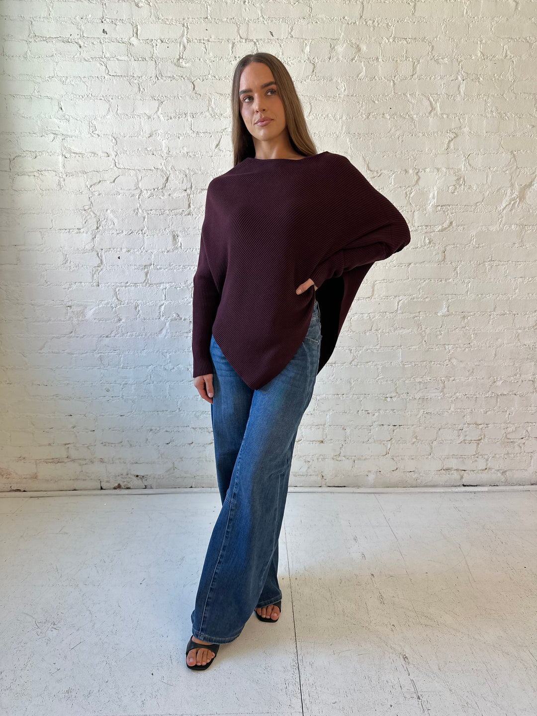 Woman wearing burgundy ribbed long sleeve sweater with pointed hem, and dark wash jean. 