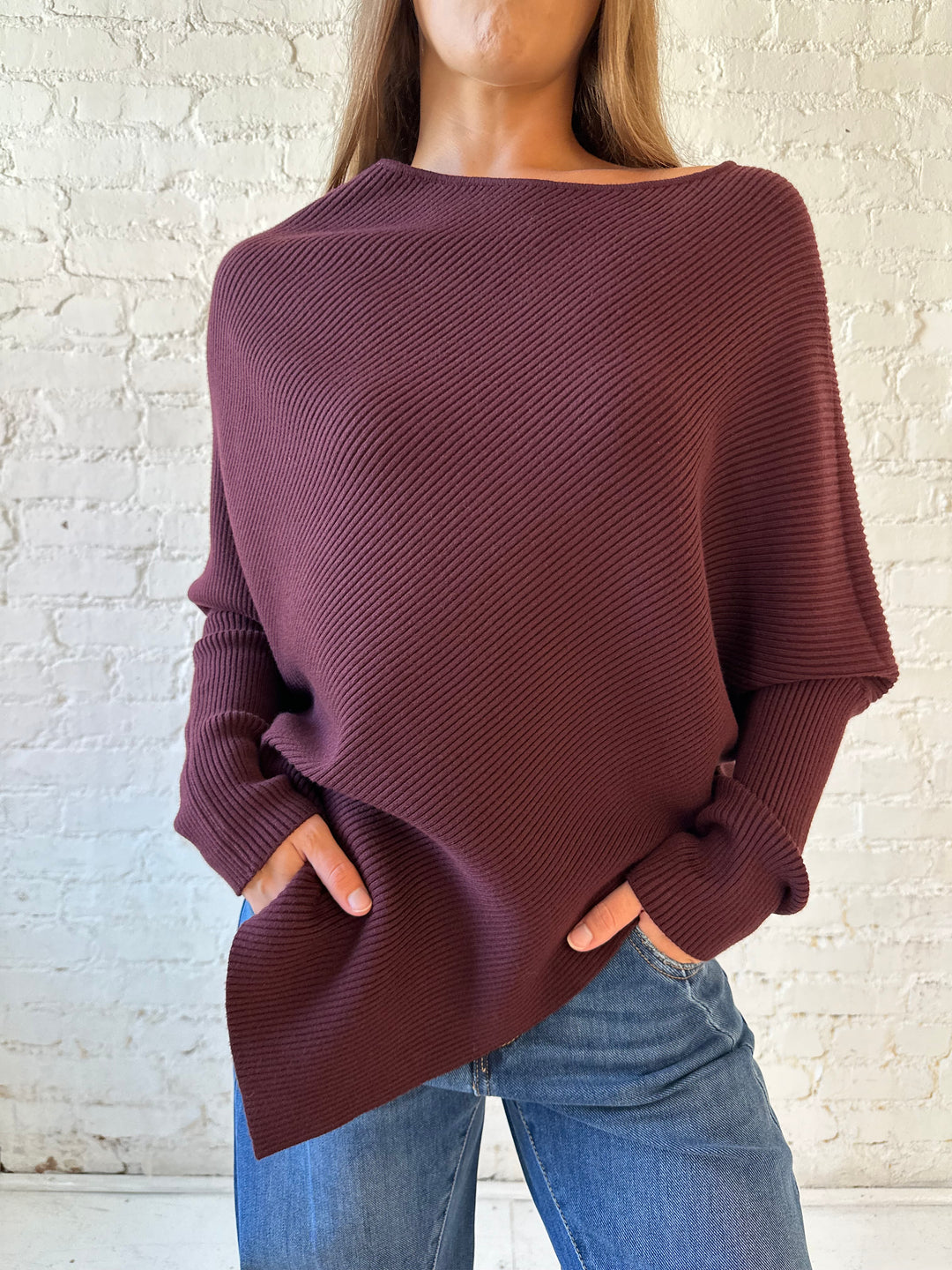 Woman wearing burgundy ribbed long sleeve sweater with pointed hem, and dark wash jean. 
