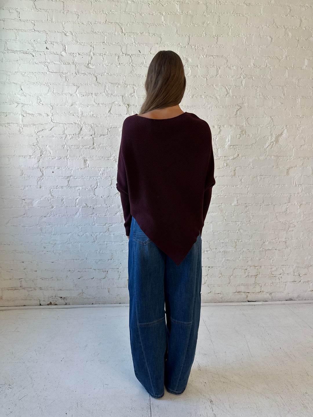 Woman wearing burgundy ribbed long sleeve sweater with pointed hem, and dark wash jean. 