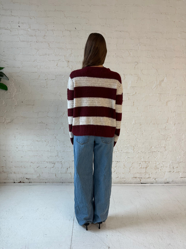 Woman wearing ivory and burgundy chunky striped zip up jacket with medium wash jeans. 