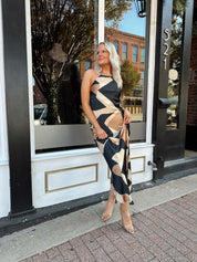 Woman wearing satin abstract pattern maxi dress with open back and halter neckline.