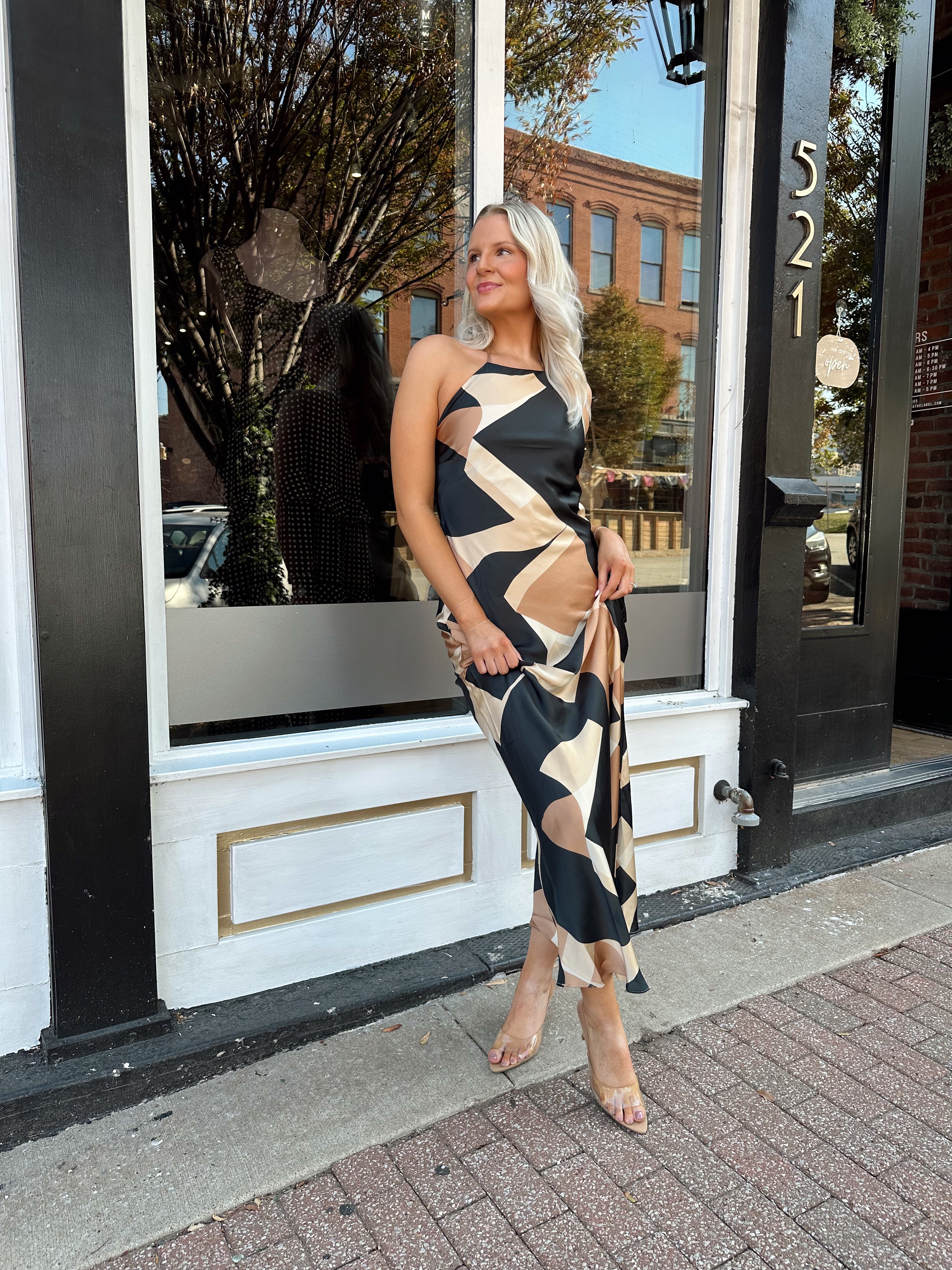 Woman wearing satin abstract pattern maxi dress with open back and halter neckline.