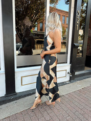 Woman wearing satin abstract pattern maxi dress with open back and halter neckline.