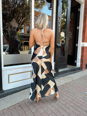 Woman wearing satin abstract pattern maxi dress with open back and halter neckline.