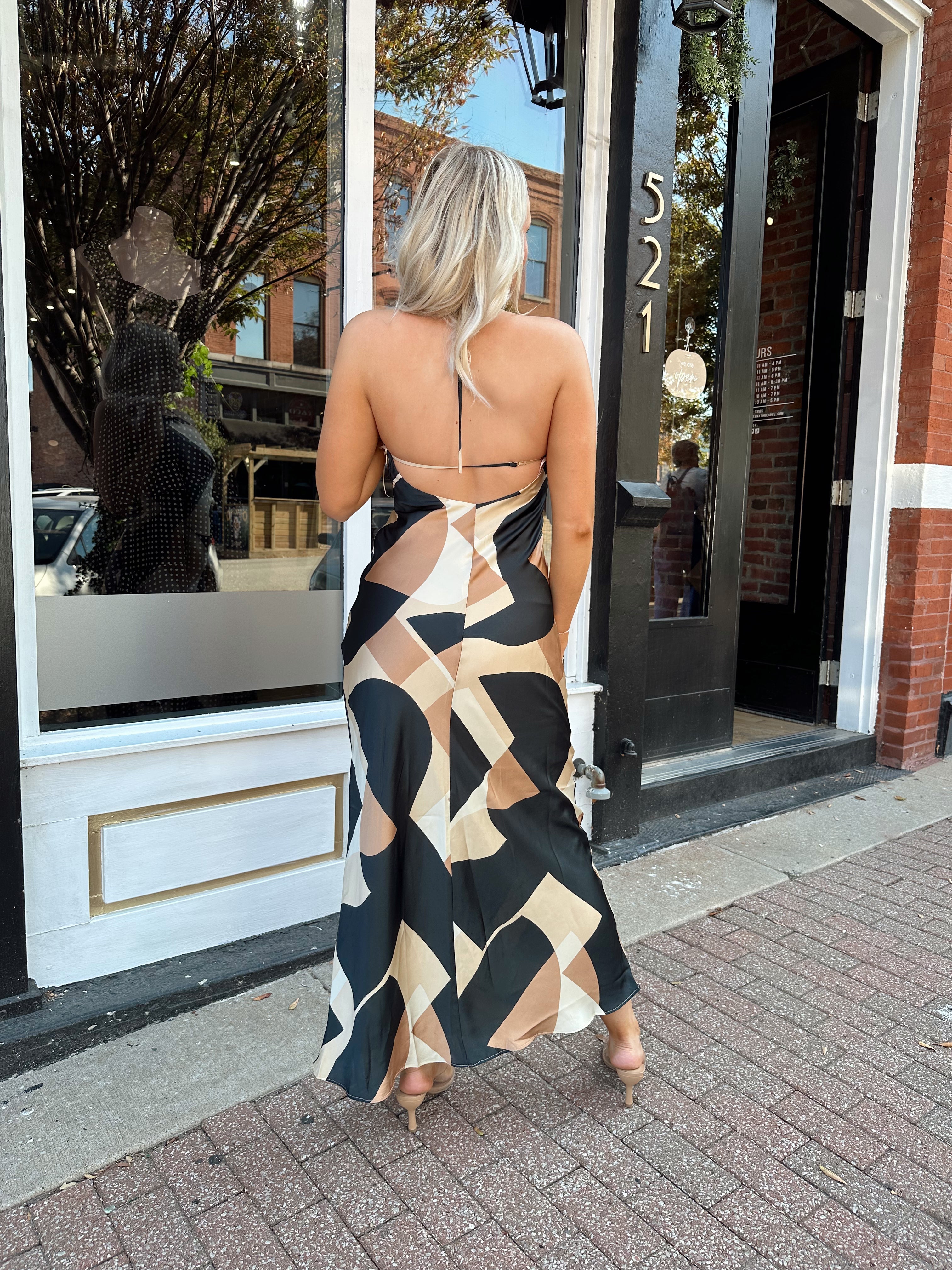 Woman wearing satin abstract pattern maxi dress with open back and halter neckline.