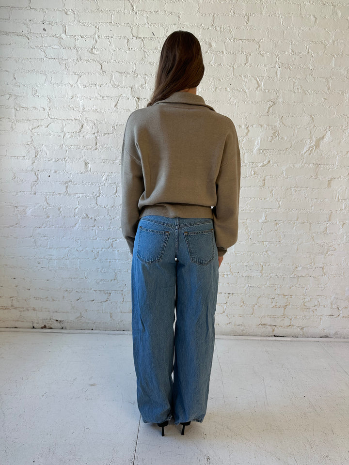 Woman wearing khaki colored knit zip up jacket with medium wash jeans. 