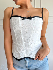 White eyelet corset with clasp closure and black trim.