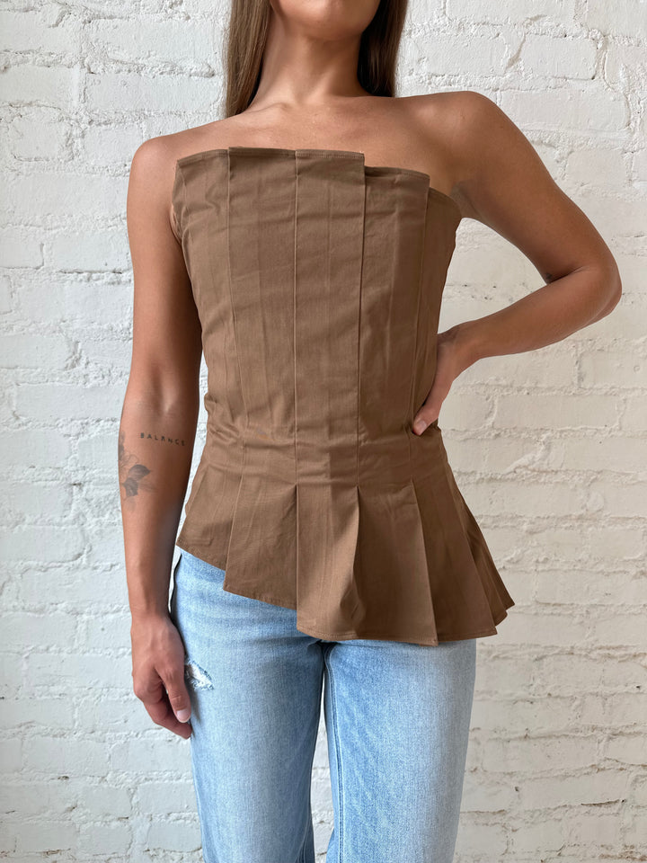 Woman wearing brown pleated asymmetrical peplum top with light wash distressed jeans.