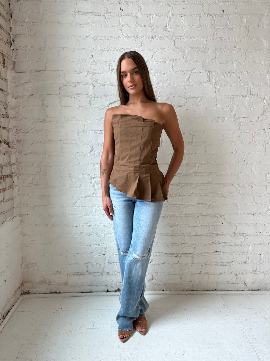Woman wearing brown pleated asymmetrical peplum top with light wash distressed jeans.
