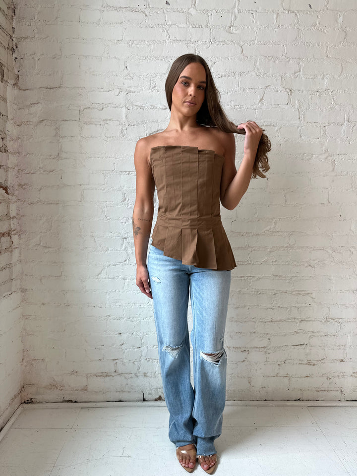 Woman wearing brown pleated asymmetrical peplum top with light wash distressed jeans.