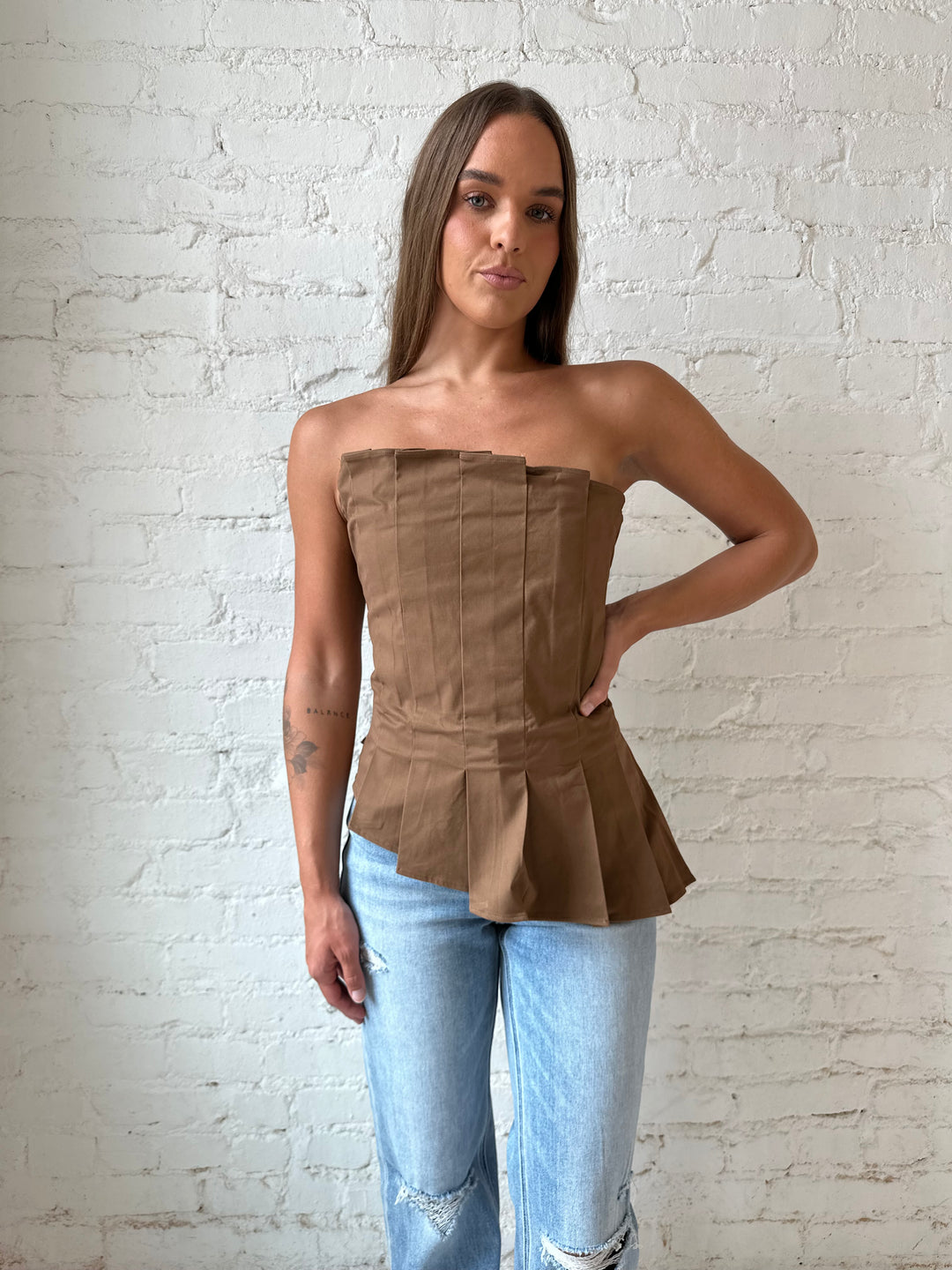 Woman wearing brown pleated asymmetrical peplum top with light wash distressed jeans.