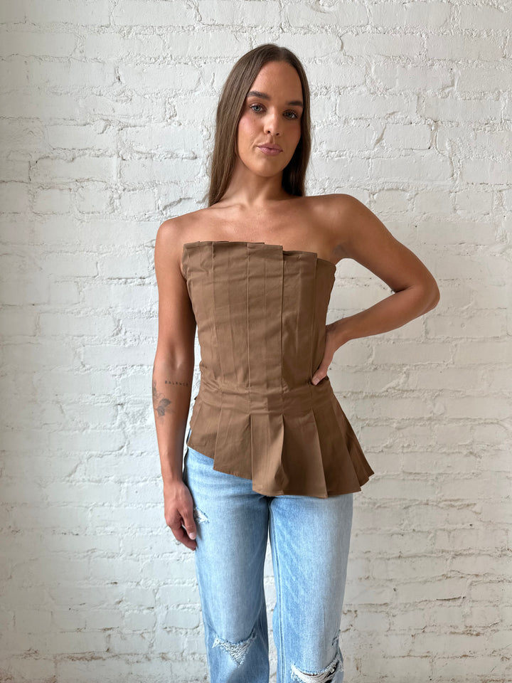 Woman wearing brown pleated asymmetrical peplum top with light wash distressed jeans.