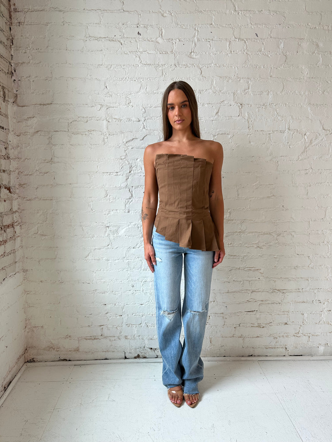Woman wearing brown pleated asymmetrical peplum top with light wash distressed jeans.