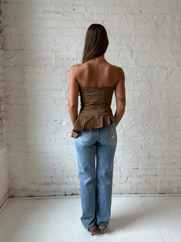 Woman wearing brown pleated asymmetrical peplum top with light wash distressed jeans.