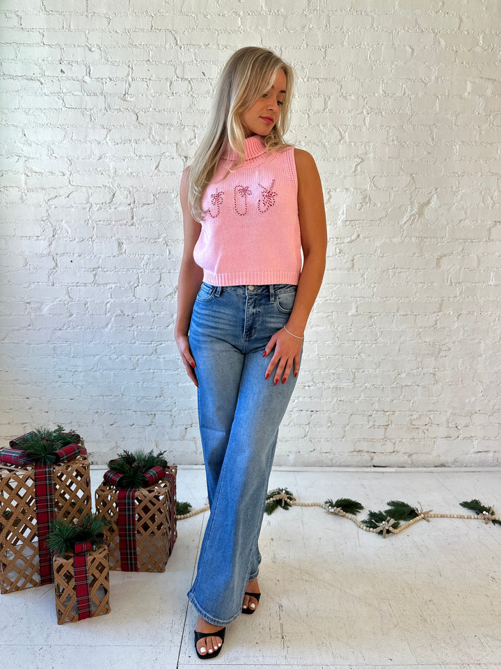 Woman wearing pink sleeveless knit turtleneck top with joy written across the front. 