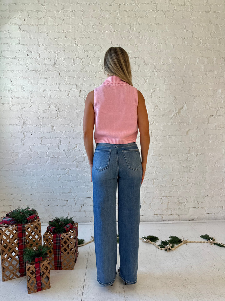 Woman wearing pink sleeveless knit turtleneck top with joy written across the front. 