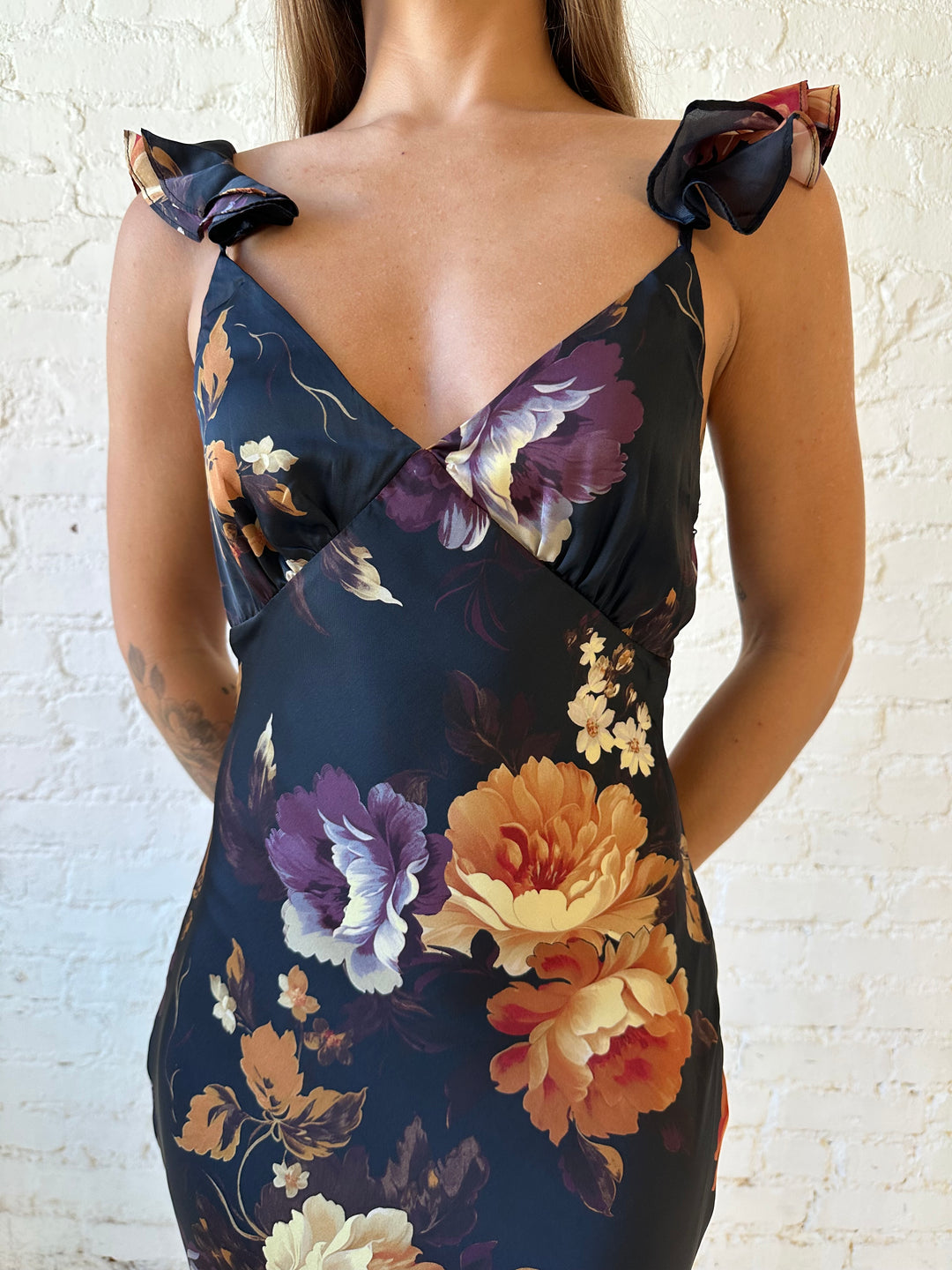 Woman wearing black floral satin maxi dress with v-neckline, ruffle, adjustable spaghetti straps, and open back.