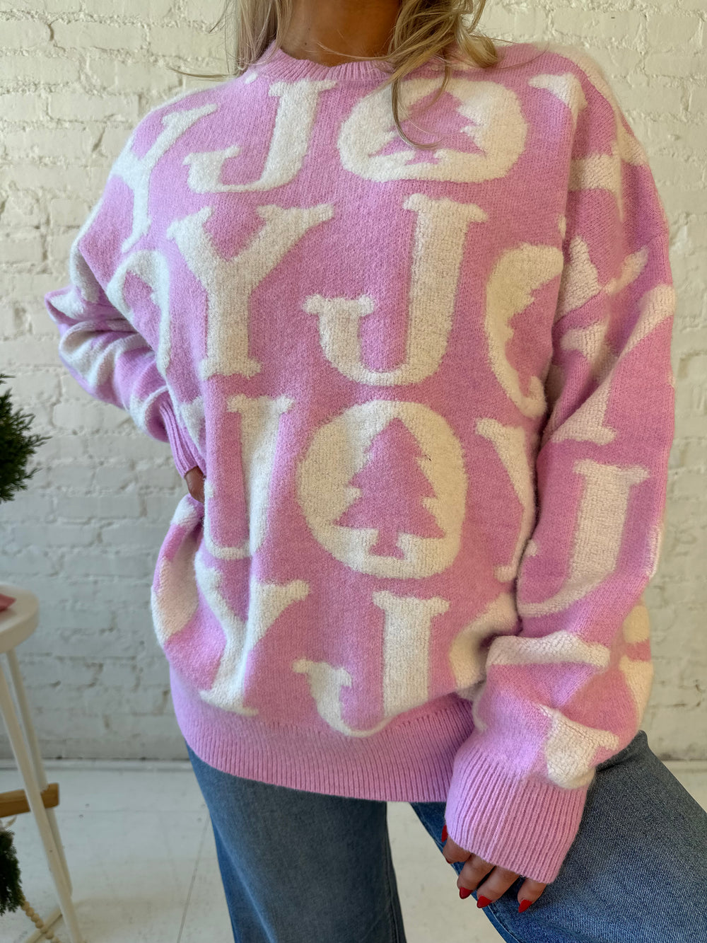 Woman wearing lilac purple oversized crewneck sweater with "Joy" written all over. 