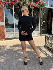 Woman wearing black long sleeve mini dress with black heels. 