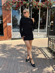 Woman wearing black long sleeve mini dress with black heels. 