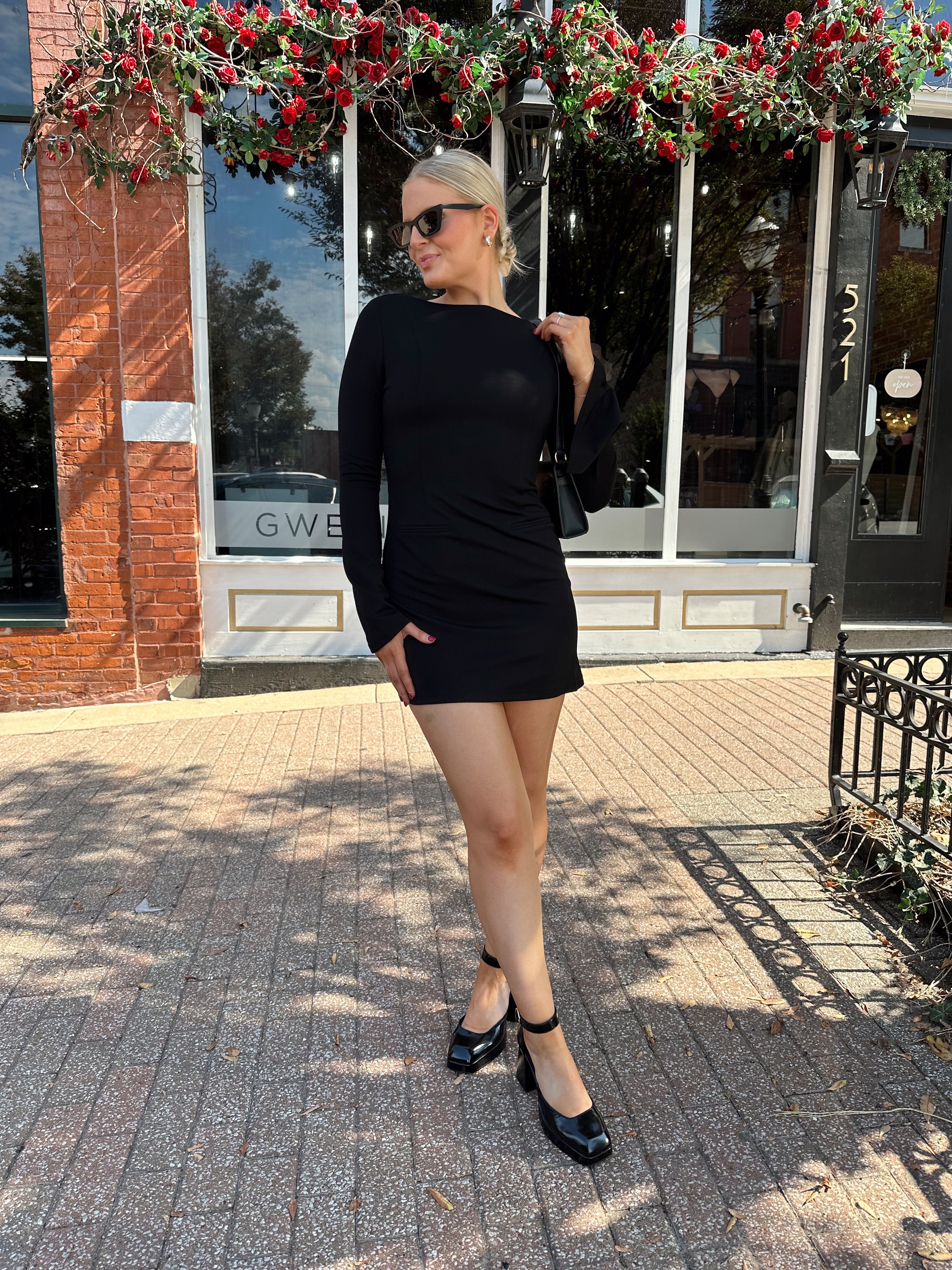 Woman wearing black long sleeve mini dress with black heels. 
