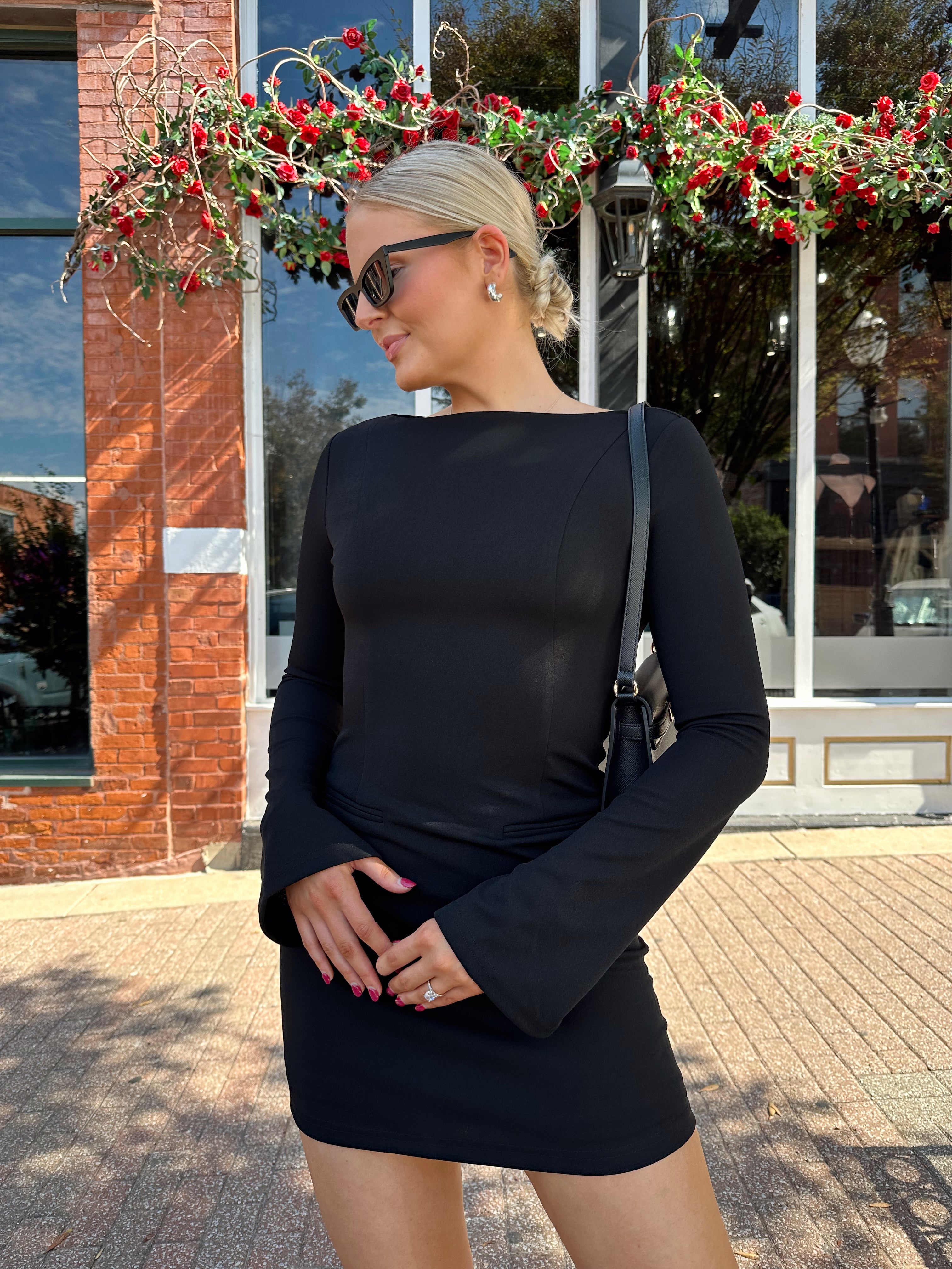 Woman wearing black long sleeve mini dress with black heels. 