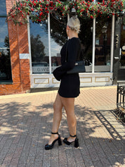 Woman wearing black long sleeve mini dress with black heels. 