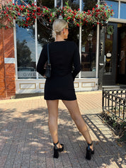 Woman wearing black long sleeve mini dress with black heels. 