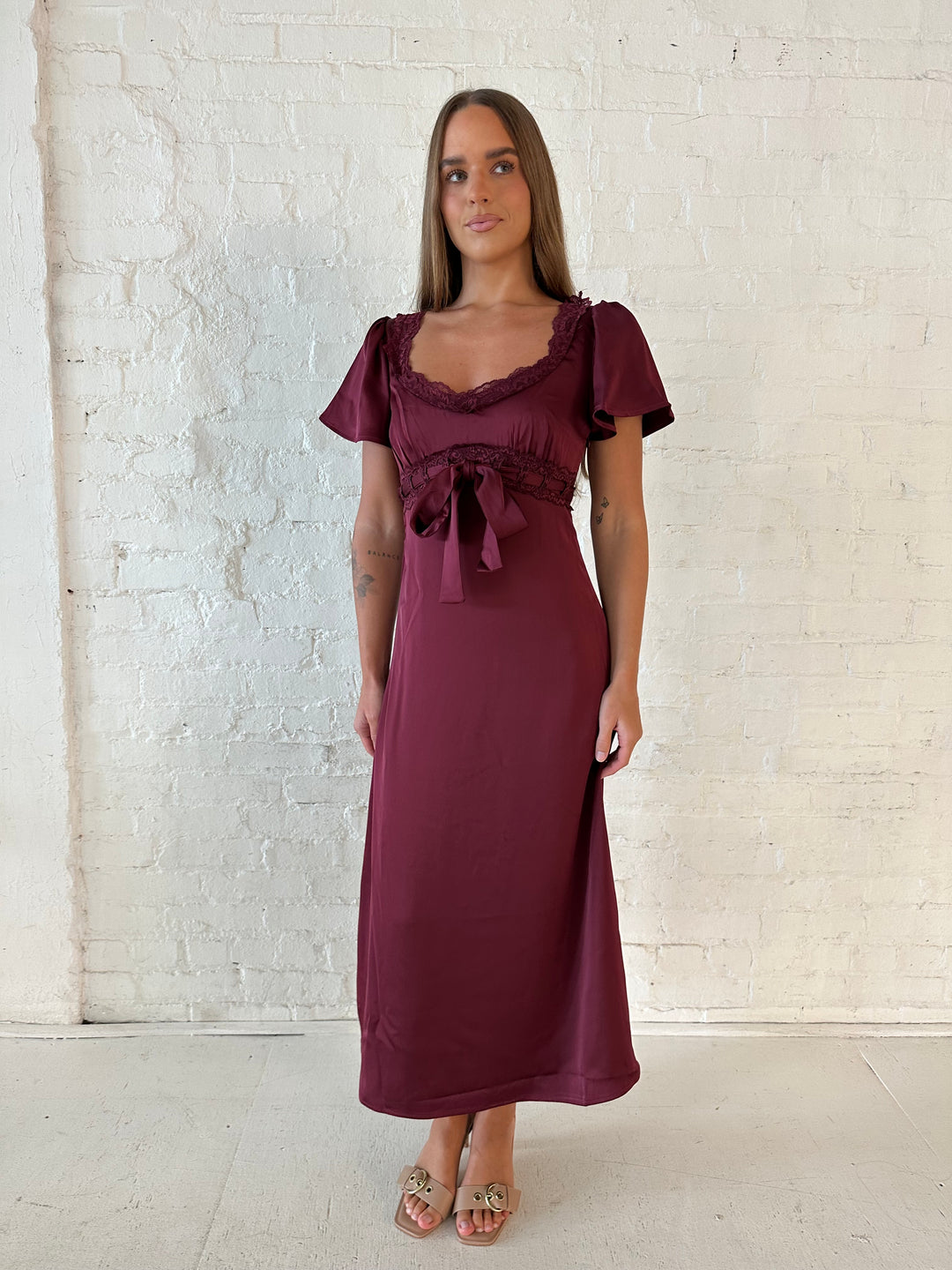 Woman wearing burgundy satin midi dress with lace trim, and self tie detail.