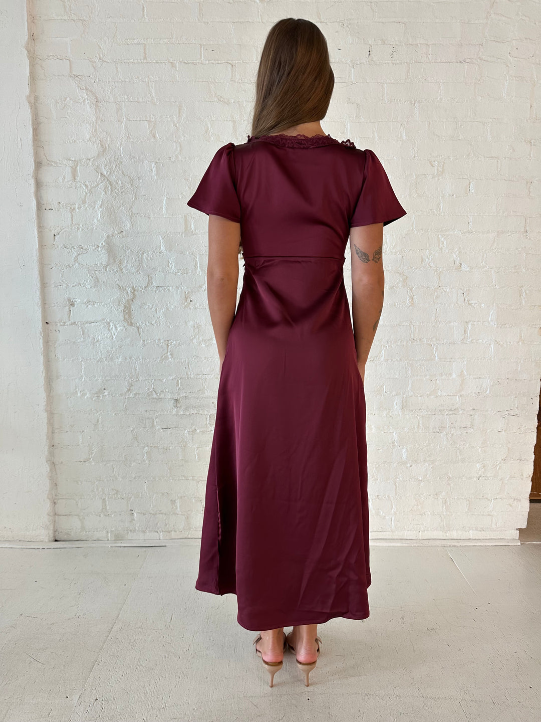 Woman wearing burgundy satin midi dress with lace trim, and self tie detail.