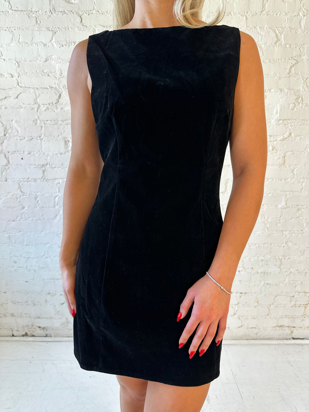 Woman wearing black velvet a-line mini dress with v-back, and black. heels. 