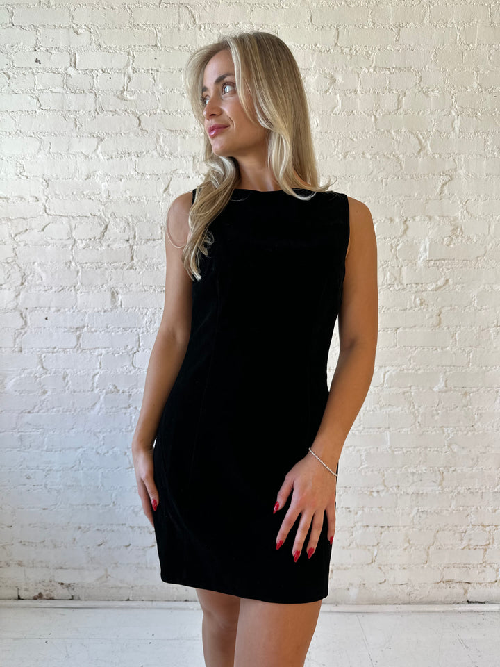 Woman wearing black velvet a-line mini dress with v-back, and black. heels. 