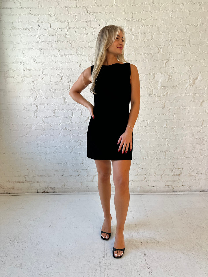 Woman wearing black velvet a-line mini dress with v-back, and black. heels. 