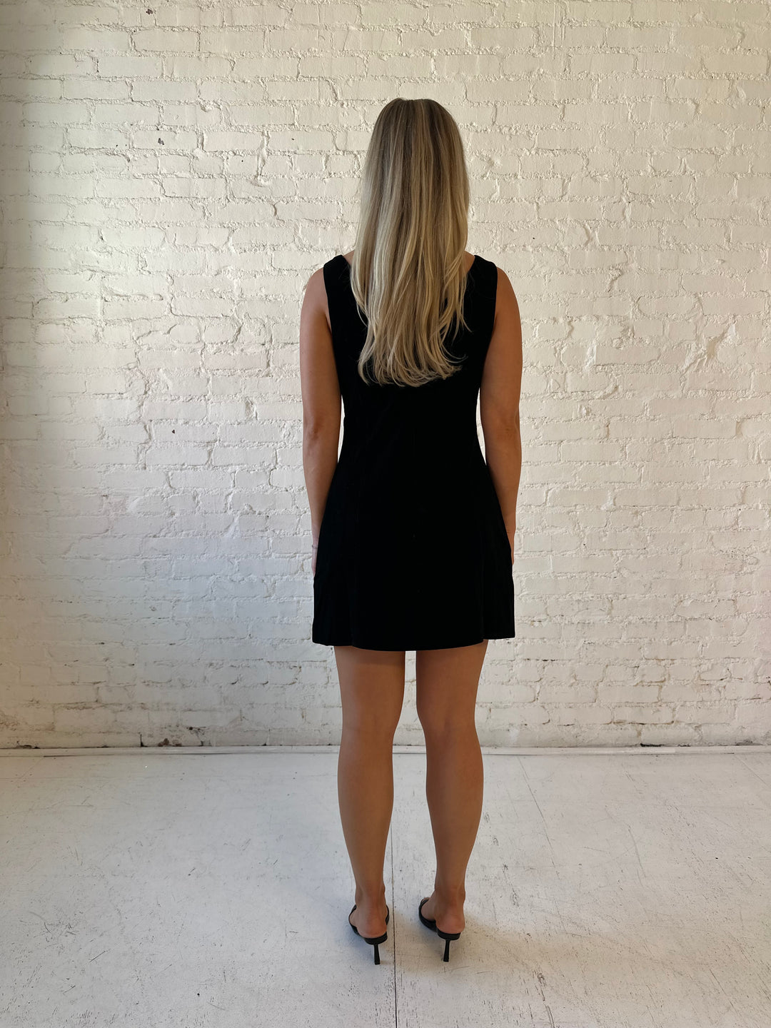 Woman wearing black velvet a-line mini dress with v-back, and black. heels. 