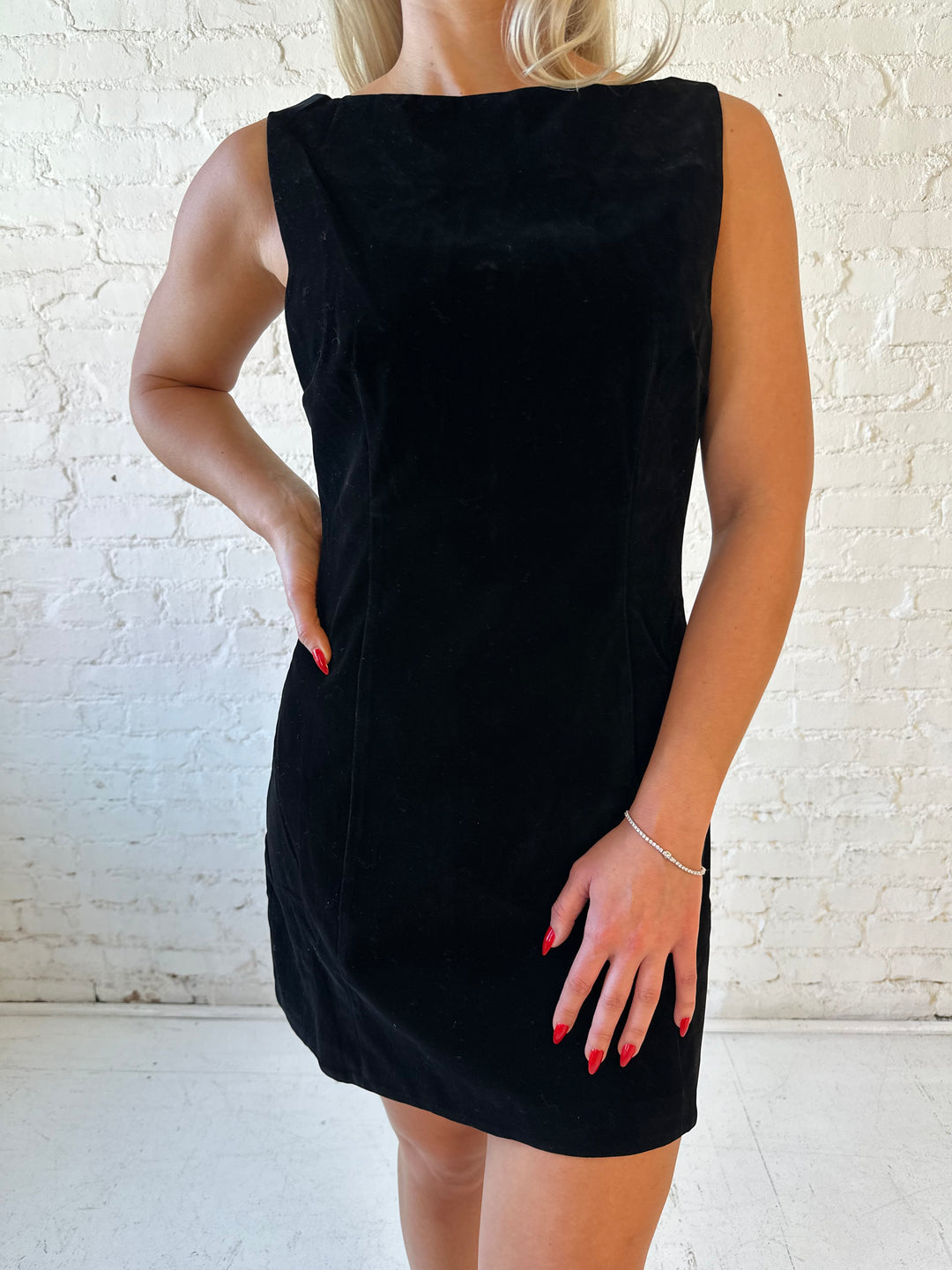 Woman wearing black velvet a-line mini dress with v-back, and black. heels. 