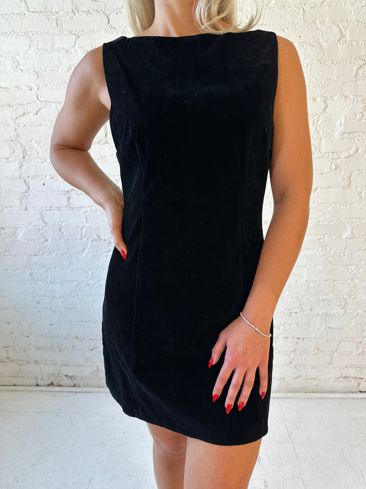 Woman wearing black velvet a-line mini dress with v-back, and black. heels. 