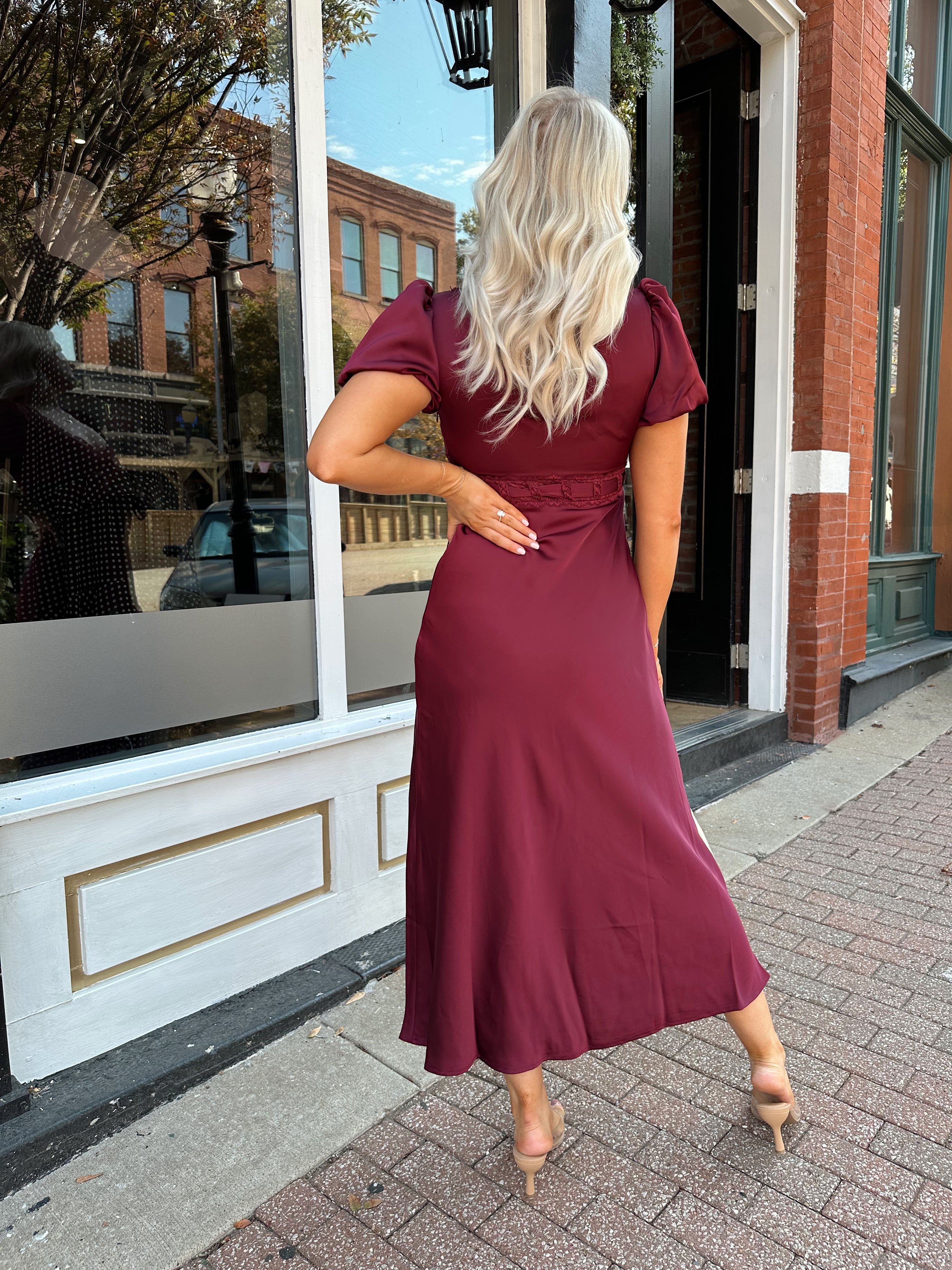 Woman wearing burgundy satin midi dress with puff sleeve, and lace detailing.
