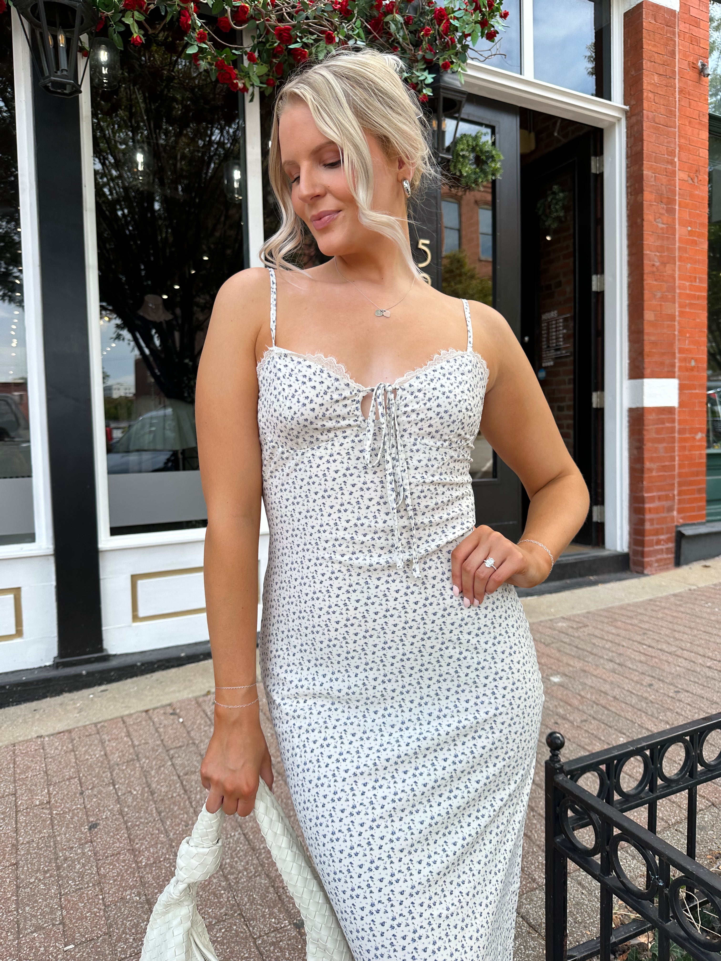 Woman wearing cream midi dress with blue floral pattern with lace trim detail. 