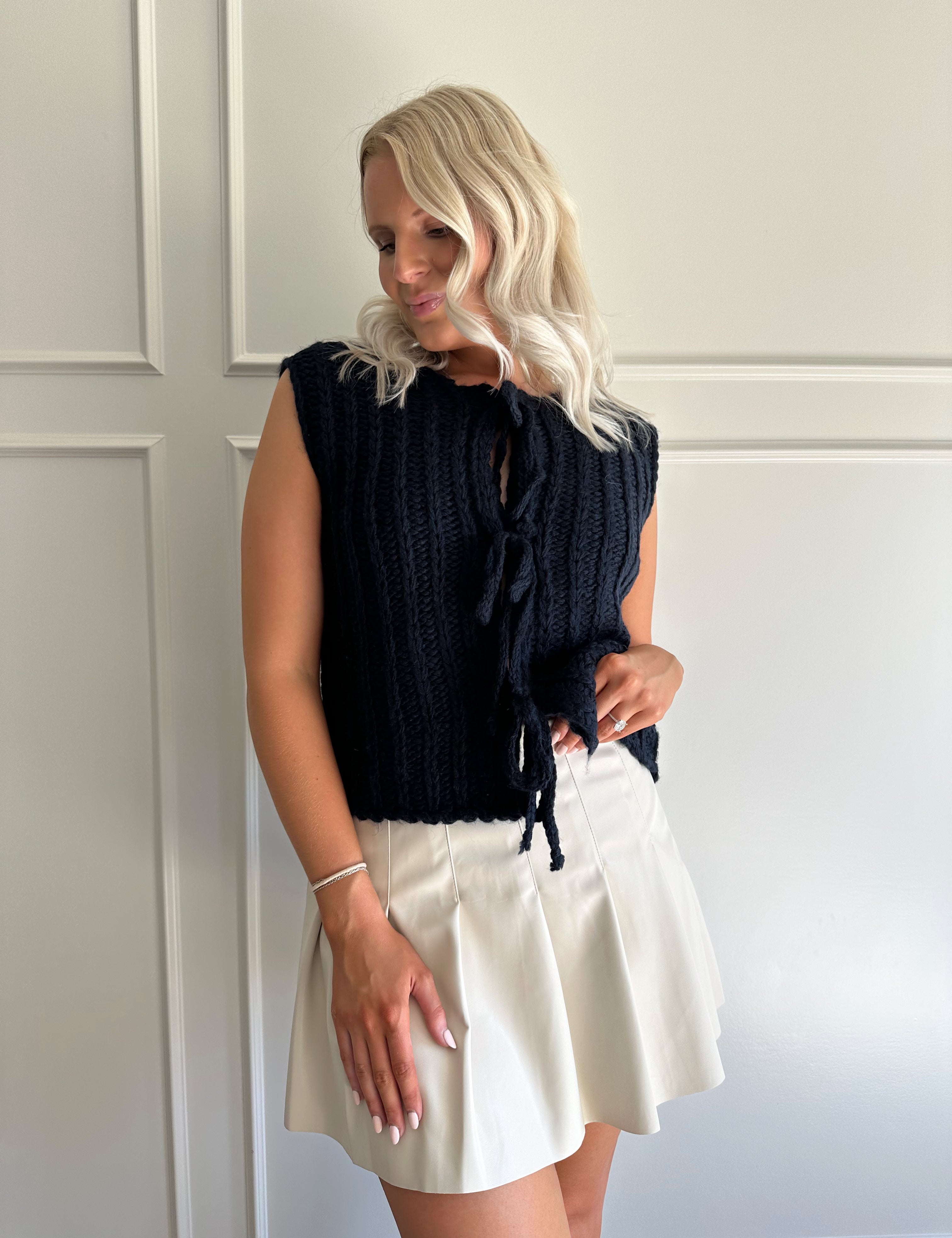 Woman wearing chunky navy blue sweater vest with tie closure and leather mini skirt. 