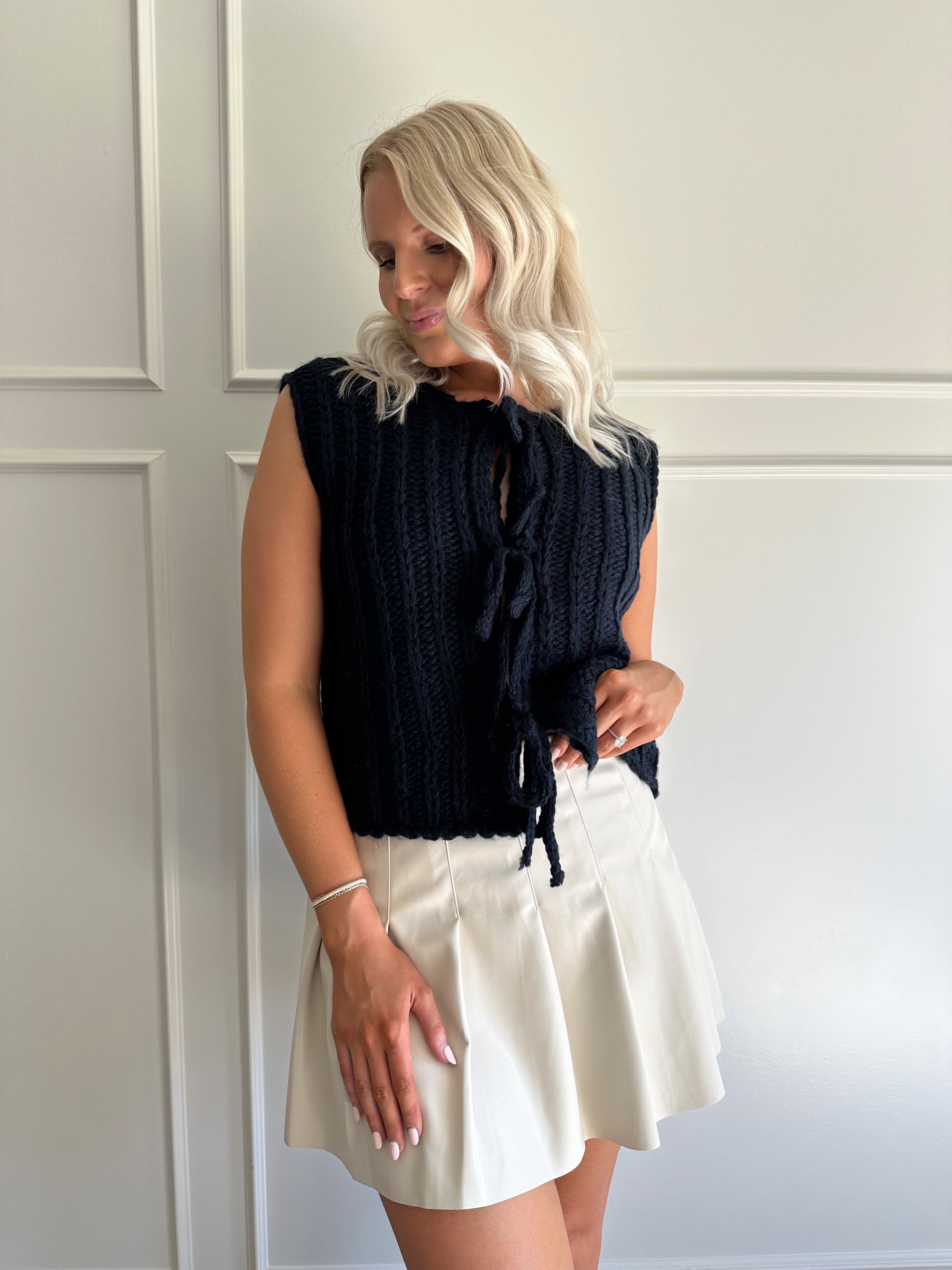 Woman wearing chunky navy blue sweater vest with tie closure and leather mini skirt. 