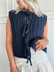 Woman wearing chunky navy blue sweater vest with tie closure and leather mini skirt. 
