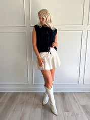 Woman wearing chunky navy blue sweater vest with tie closure and leather mini skirt. 
