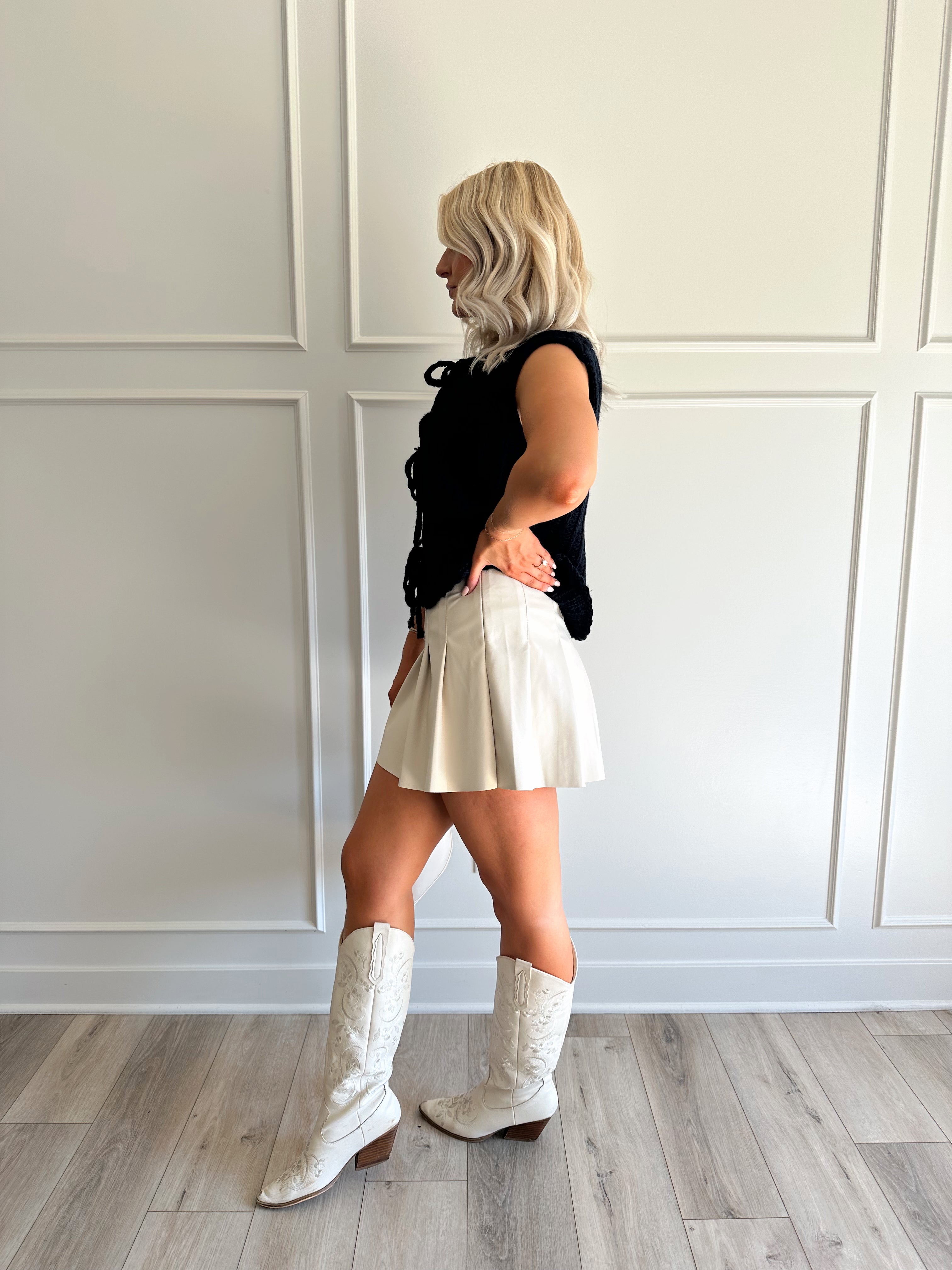 Woman wearing chunky navy blue sweater vest with tie closure and leather mini skirt. 