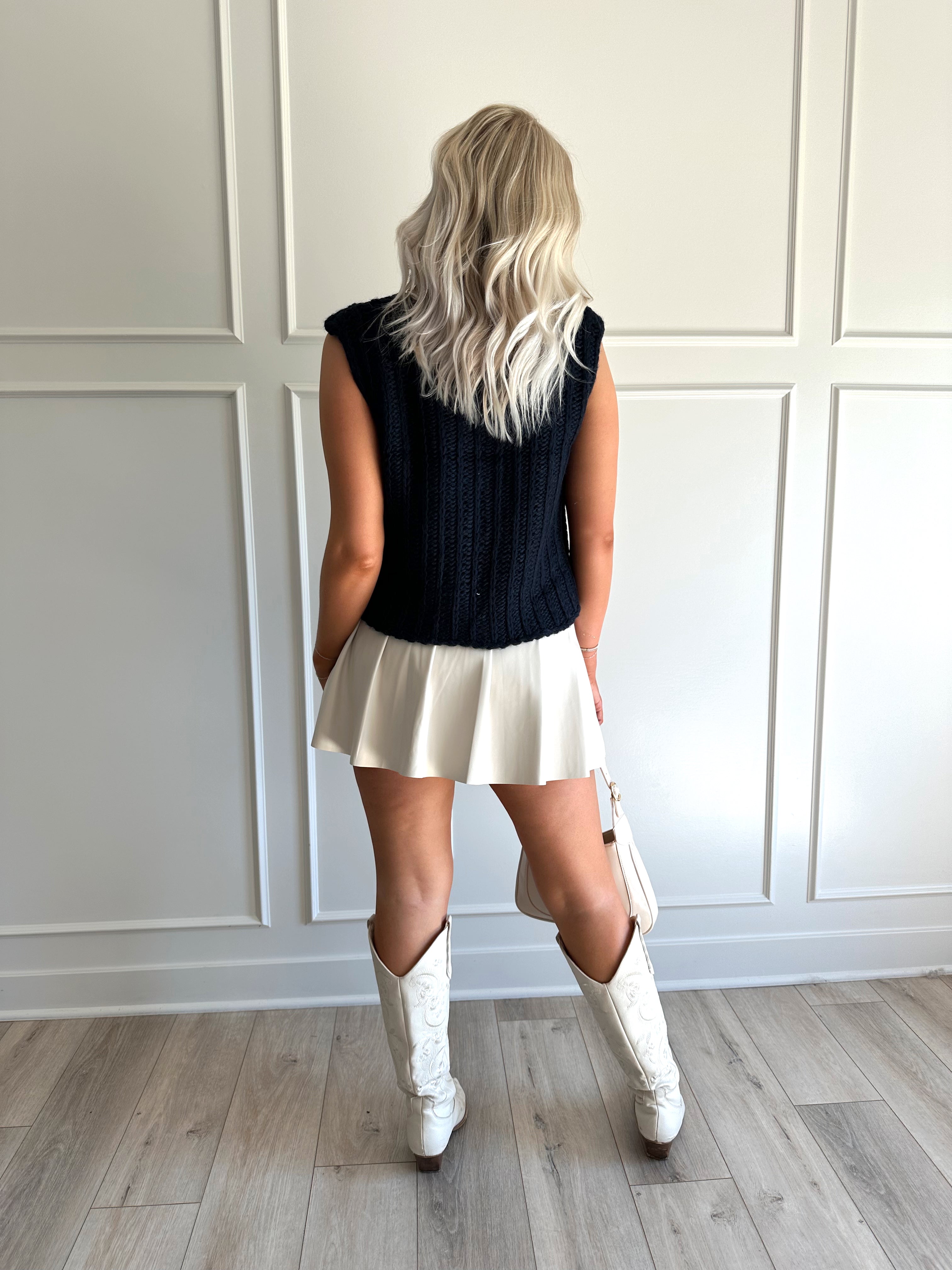 Woman wearing chunky navy blue sweater vest with tie closure and leather mini skirt. 