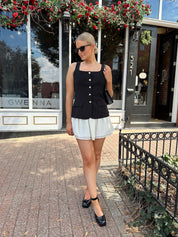 Woman wearing black tailored mini dress with white overlay poking out and gold button closure. 