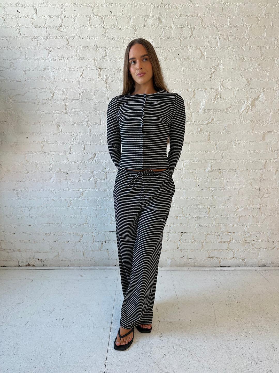 Woman wearing black striped two piece lounge set with button down long sleeve top.